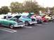 1989 Ford Mustang - A row of vintage vehicles, including a green panel van, are parked in a lot with their hoods open.