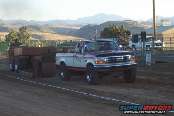 Ford pickup truck pulling a sled on a dirt track, mountains in background