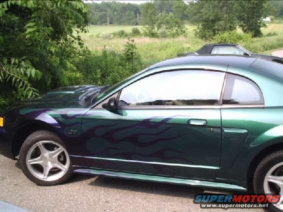 Green Ford Mustang coupe with purple flame graphics on the side, showing the front wheel and part of the hood