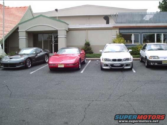 Four cars parked in a lot: a dark gray Dodge Viper, a red Chevrolet Corvette, a silver BMW, and a white Ford Mustang