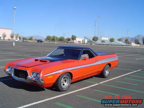 Orange 1973 Ford Ranchero parked in an empty lot, black vinyl top, silver stripe on side