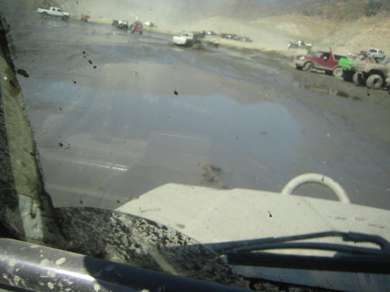 Muddy windshield view of off-road vehicles in a dirt landscape
