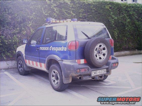 Rear view of a blue and white police SUV with 'mossos d'esquadra' text and red and white stripes. Spare tire mounted on the back