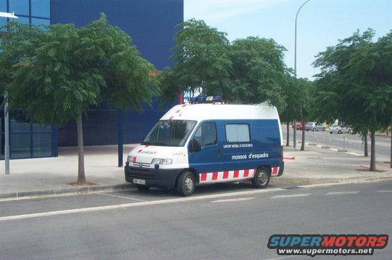 White and blue police van with red and white striped lower body, parked on a street