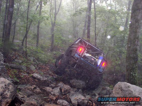 Off-road vehicle with roll cage tilted on rocky terrain, red taillights illuminated
