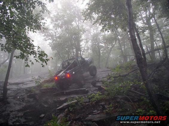 off-road buggy climbing a steep, rocky, wooded trail on a foggy day