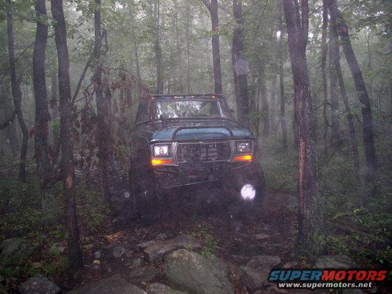 Green Ford Bronco navigating rocky terrain in a misty forest
