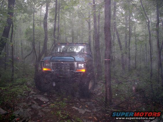 Muddy Ford Bronco on rocky trail in foggy woods. Another vehicle visible in distance