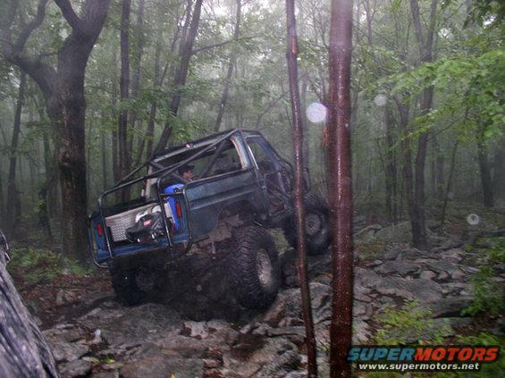 Blue off-road SUV with roll cage navigating rocky terrain