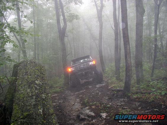 Ford Bronco driving on a muddy, rocky trail through a foggy forest