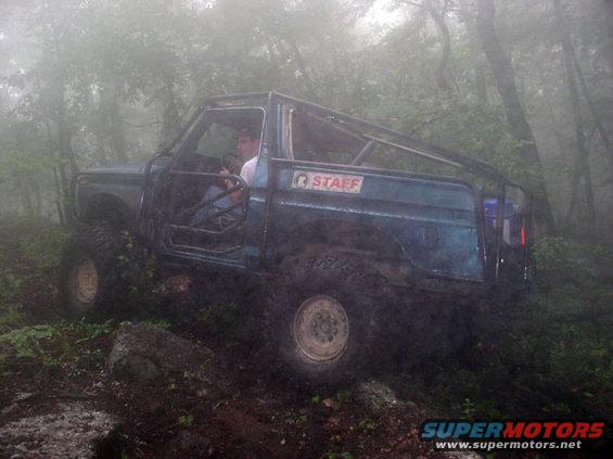 Off-road vehicle with a roll cage driving through a foggy forest. A person is in the driver's seat