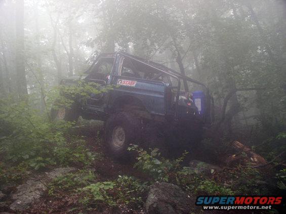 Blue off-road SUV with roll cage on rocky terrain in fog