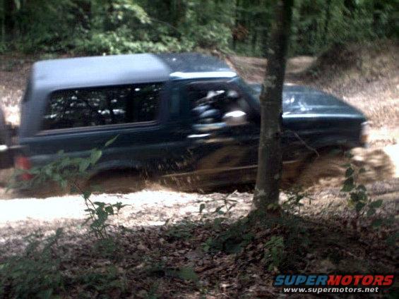 Dark green Ford Bronco driving through mud on a wooded trail