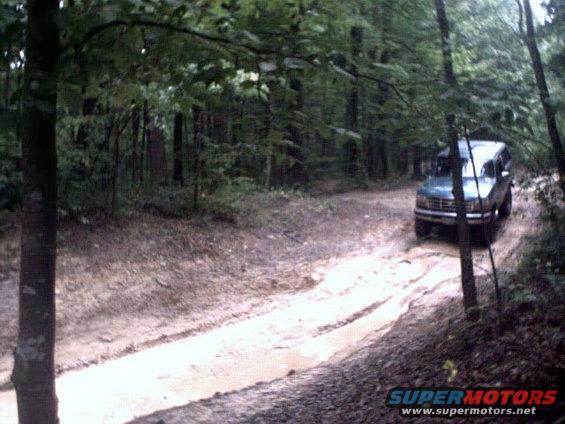 Dark blue Ford Bronco driving on a muddy forest road