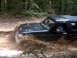 1996 Ford Bronco - A 1996 Ford Bronco navigates a muddy trail, kicking up dirt and water.