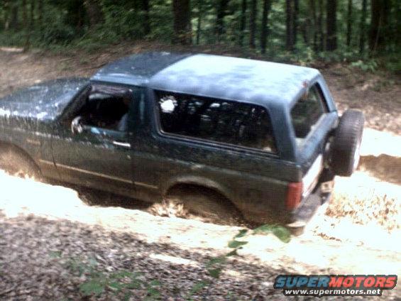 Dark green 1996 Ford Bronco driving through mud, rear spare tire visible