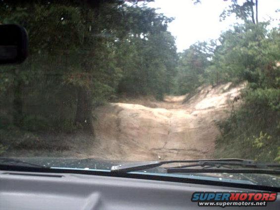 View from inside a vehicle looking out at a muddy, rutted dirt road going uphill through a forest