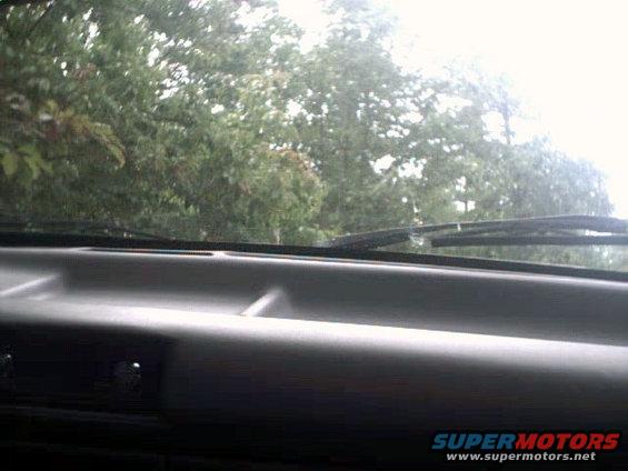 Looking out the windshield from inside a vehicle, showing the dashboard and trees outside