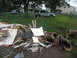 1995 Ford C-350 (Centurion Conversions) - Debris and logs are piled up in front of a fence, with houses and vehicles visible beyond.