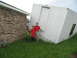 1995 Ford C-350 (Centurion Conversions) - A damaged portable building is tilted on its side next to a brick house after a storm.