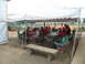 1995 Ford C-350 (Centurion Conversions) - A group of people are gathered under a large white tent, seated at tables and chairs, with a baseball field visible in the background.