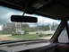 1995 Ford C-350 (Centurion Conversions) - View from inside a vehicle, looking out through a rain-streaked windshield at a gas station and surrounding trees.
