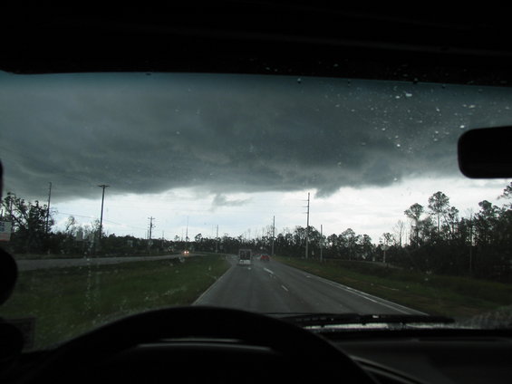 View from inside a vehicle looking out at a dark, stormy sky over a highway with trees on the side