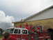 1995 Ford C-350 (Centurion Conversions) - A fire truck with several children on its roof stands in front of a yellow brick building under a cloudy sky.