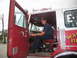 1995 Ford C-350 (Centurion Conversions) - A firefighter sits in the cab of a red fire truck, with the driver's side door open.
