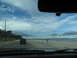 1995 Ford C-350 (Centurion Conversions) - View from inside a vehicle driving down a road beside a sandy beach with the ocean in the distance.