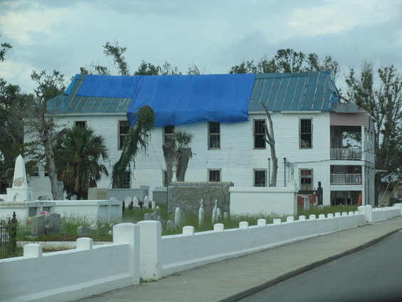 White building with blue tarp on roof, next to a cemetery with gravestones