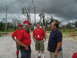 1995 Ford C-350 (Centurion Conversions) - Men in red shirts and a man in a blue shirt stand and talk outside with a trailer in the background.