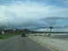 1995 Ford C-350 (Centurion Conversions) - A dark SUV drives down a road with a speed limit sign and storm-damaged trees under a cloudy sky.