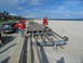 1995 Ford C-350 (Centurion Conversions) - A group of people stand on and near a damaged boardwalk on a beach, with a blue SUV parked nearby.