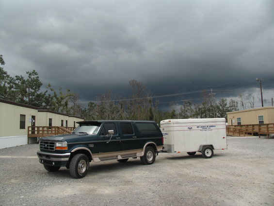 Dark green Ford Bronco towing a white trailer with 'Boy Scouts of America' on it, under a stormy sky