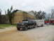 1995 Ford C-350 (Centurion Conversions) - A Ford SUV tows a trailer near a damaged yellow building, with several people in red shirts gathered around.