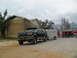 1995 Ford C-350 (Centurion Conversions) - A dark green SUV tows a white trailer past a yellow brick building.