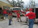 1995 Ford C-350 (Centurion Conversions) - A group of people, some wearing red shirts, are gathered around a fire truck and a trailer.
