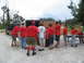 1995 Ford C-350 (Centurion Conversions) - An extended cab pickup truck is parked next to a trailer while a group of people in red shirts unload supplies.
