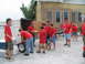 1995 Ford C-350 (Centurion Conversions) - People in red shirts are seen unloading supplies from a trailer in front of a brick building.