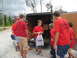 1995 Ford C-350 (Centurion Conversions) - A group of boys are seen helping to unload items from the back of a trailer.