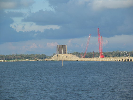 Bridge construction scene with two red cranes over water