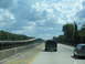 1995 Ford C-350 (Centurion Conversions) - A view from a vehicle traveling on a highway, showing an elevated bridge and other cars on the road under a cloudy sky.