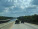 1995 Ford C-350 (Centurion Conversions) - Two SUVs travel on a highway that crosses over a body of water, with a bridge construction project visible to the left.