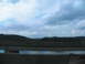 1995 Ford C-350 (Centurion Conversions) - A view from a bridge shows a concrete barrier overlooking a body of water with a rainbow sheen, under a cloudy sky.