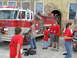 1995 Ford C-350 (Centurion Conversions) - A group of people, some wearing red shirts, stand near a large red fire truck.