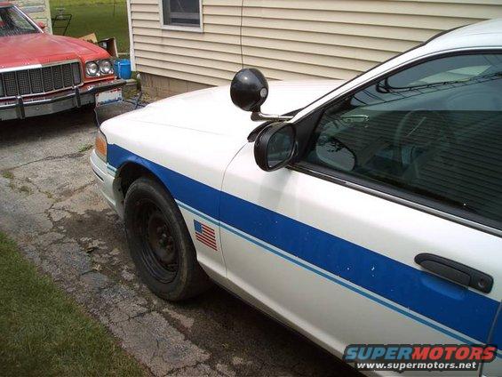 1999 Ford Crown Victoria police car with blue stripe, parked next to a red car