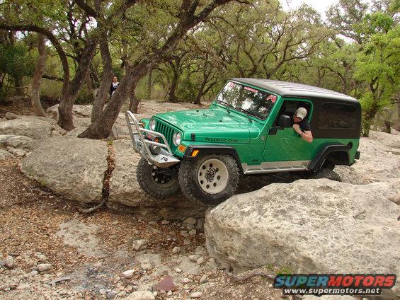 Green Jeep Wrangler Rubicon navigating large rocks on a trail