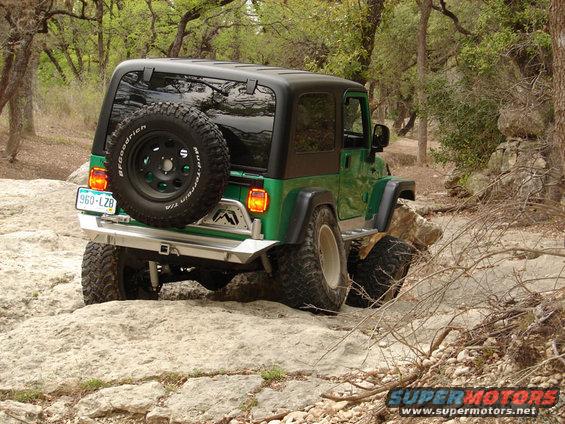 Green Jeep Wrangler with spare tire on rear, navigating rocky trail