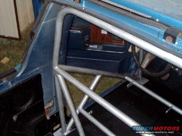 Interior of a vehicle with a silver roll cage installed. Blue door panel and wood trim visible